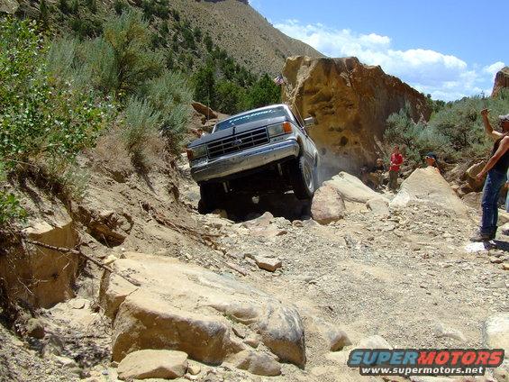 1987 Ford Bronco navigating a steep, rocky trail with people watching