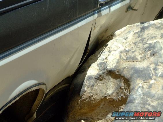 Side panel of a vehicle is bent and torn, wedged against a large rock