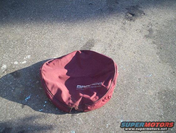 Maroon Bronco spare tire cover with "BRONCO 25th ANNIVERSARY" text on asphalt
