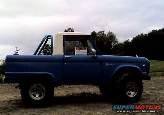 Blue 1973 Ford Bronco with a white removable top and roll bar, parked outdoors on a dirt lot