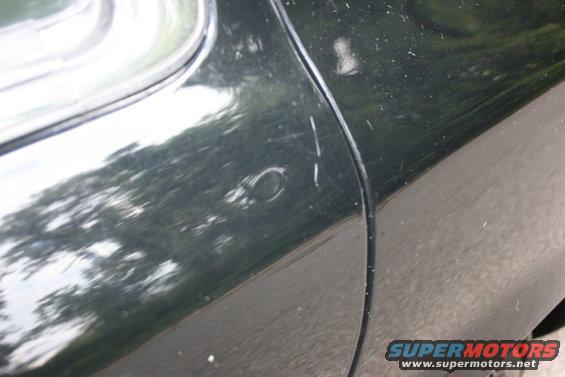 Dark green car door with scratches and a small dent near the panel gap