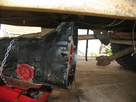 vehicle transmission and driveshaft removed from under a vehicle, resting on a red jack stand