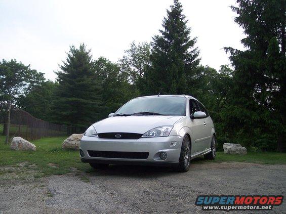 Silver 2003 Ford Focus hatchback parked on gravel with trees in background