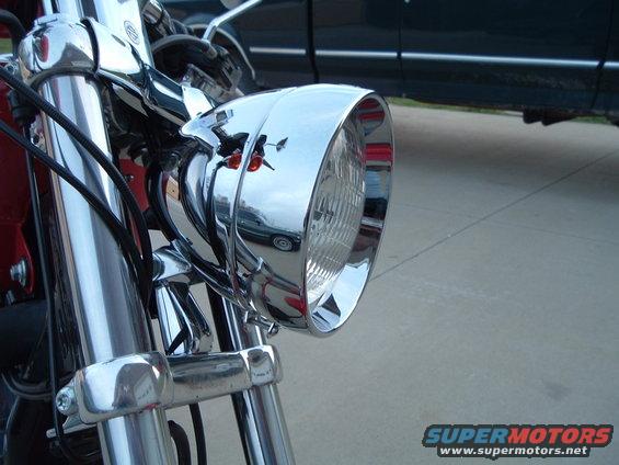 Chrome motorcycle headlight assembly with visible reflection of a dark SUV