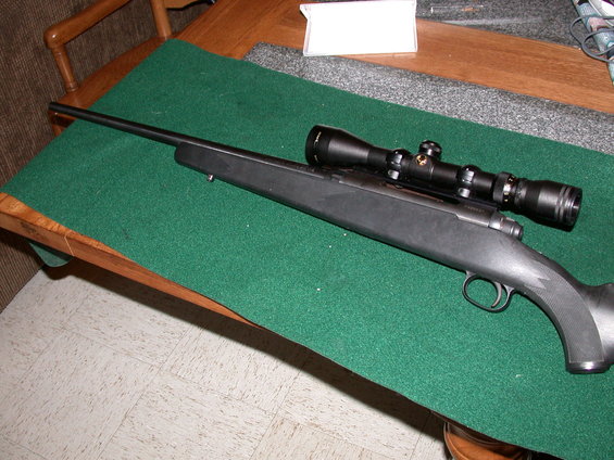 Rifle with scope on a green felt surface on a wooden table