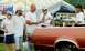 1976 Ford Ranchero - Several people are gathered near the back of an orange vehicle at an outdoor event.