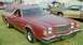 1976 Ford Ranchero - A red 1976 Ford Ranchero pickup truck with a camper shell is parked on grass, with another vehicle visible in the background.