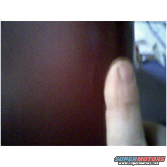Close-up of a thumb and forefinger obscuring a dark surface, with a blurry background