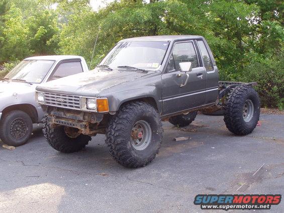 Gray Toyota pickup truck with large off-road tires, missing its bed. Another truck is parked next to it