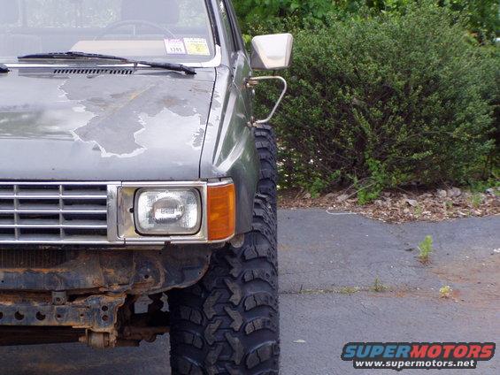 Gray truck front corner with peeling paint, large off-road tires, and a chrome grille