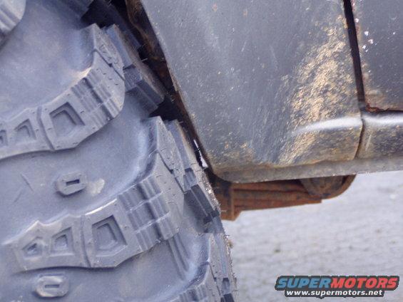 Close-up of a large off-road tire next to a vehicle's fender and leaf spring