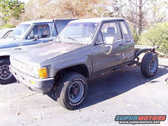 1985 Toyota pickup truck chassis with cab and front end, rear frame removed. Another truck is parked behind it