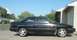 1989 Mazda MX-6 - A black coupe is parked in a driveway on a sunny day, with a house and trees in the background.