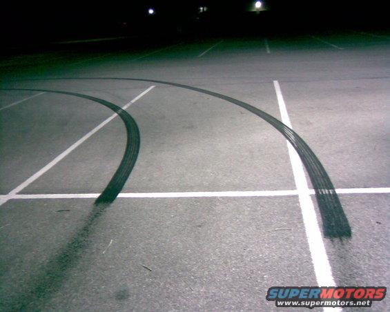 Tire marks on asphalt in a parking lot at night. White lines mark parking spaces