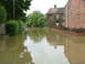 2001 Ford Fiesta - A street is submerged in floodwaters, with houses lining the sides and a person wading through the water.