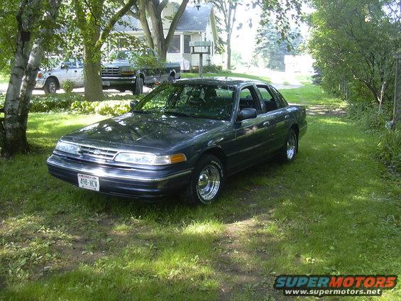Dark sedan parked on grass, with a pickup truck and another vehicle in the background