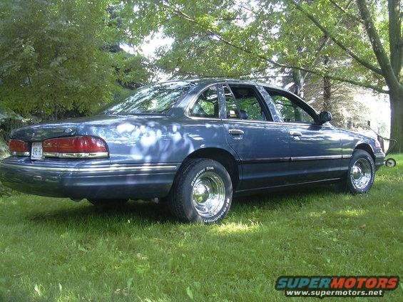 Blue sedan parked on grass, rear quarter view. Chrome wheels and trim visible