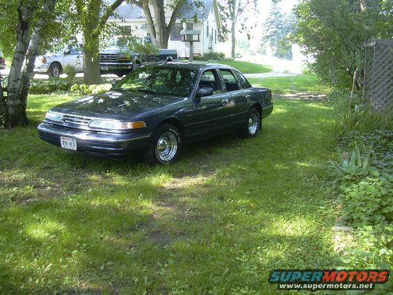 Dark sedan parked on grass with a white pickup truck in the background