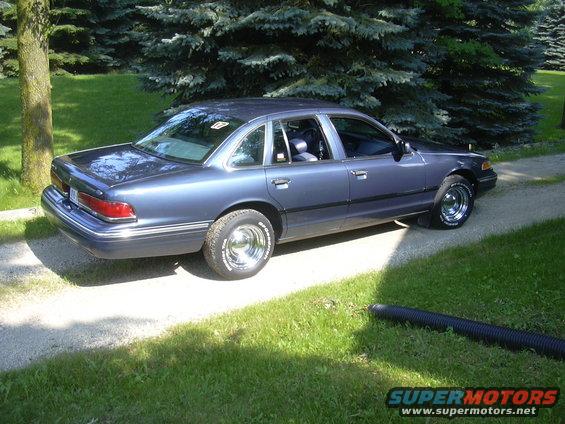 Blue Ford Crown Victoria parked on a gravel driveway next to a lawn and trees
