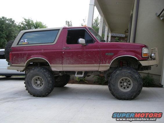 Red Ford Bronco with tan top, lifted with large tires, parked on concrete