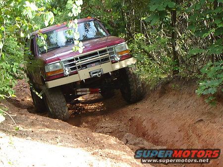 Maroon Ford Bronco off-roading on a dirt trail, showing a tan aftermarket bumper and winch