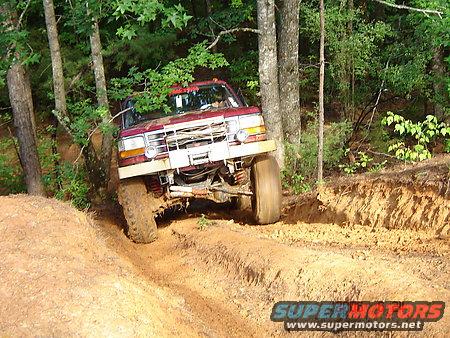 1995 Ford Bronco climbing a muddy hill in a wooded area