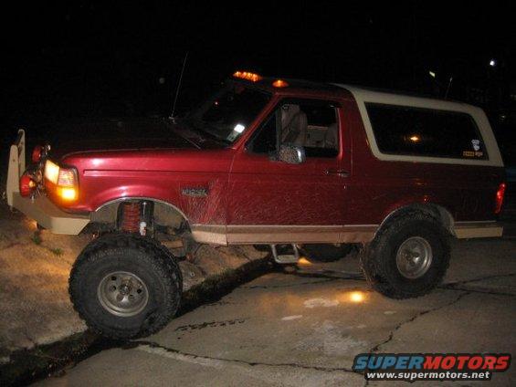 Lifted red SUV with off-road tires and custom bumper, parked at night
