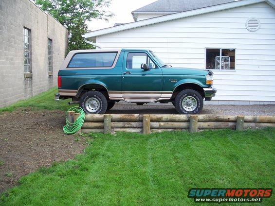 Green 1990s Ford Bronco side view parked next to a white building