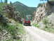 1996 Jeep Cherokee - A red Jeep Cherokee drives down a gravel road through a mountain pass on a sunny day.