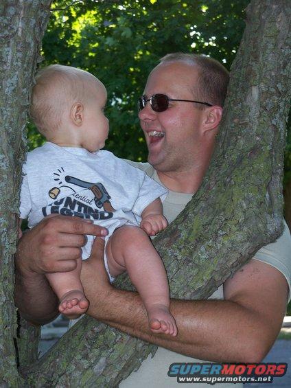 Man holding baby in a tree, baby wears shirt with gun graphic