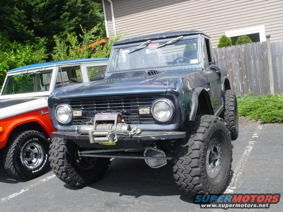 Dark blue Ford Bronco with winch and large tires parked next to an orange and white Bronco