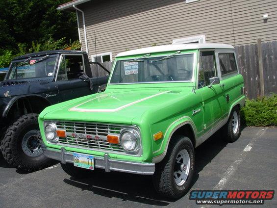 Green 1973 Ford Bronco with a white top, parked next to a dark SUV
