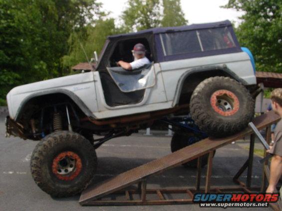 White 1973 Ford Bronco with large tires on a ramp, driver visible