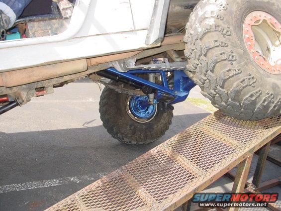 White off-road vehicle's rear suspension with blue components and large tire on a ramp