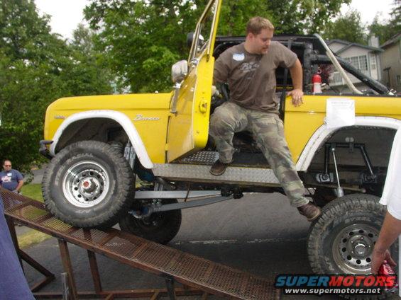 Yellow 1973 Ford Bronco, man climbing out, ramp in front