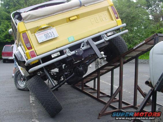Yellow Ford Bronco with a soft top is being loaded onto a trailer via a ramp. A red SUV is parked nearby
