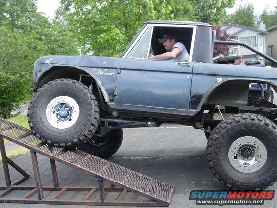 Dark blue 1973 Ford Bronco with large tires on a metal ramp, driver visible