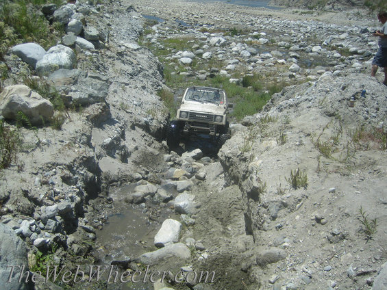 White 1987 Suzuki Samurai navigating a rocky stream bed