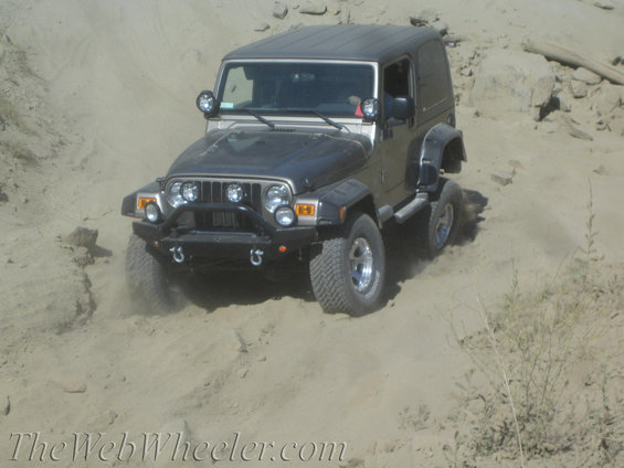 Gray Jeep Wrangler with a black hardtop driving on a sandy trail
