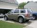 2004 Dodge Durango - A tan 2004 Dodge Durango SUV is parked in a driveway next to a garage and a blue truck.
