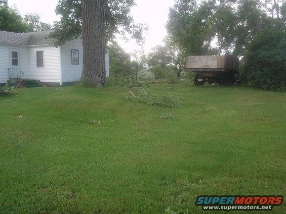 old flatbed truck parked in a yard with a house and a big tree, debris on the ground