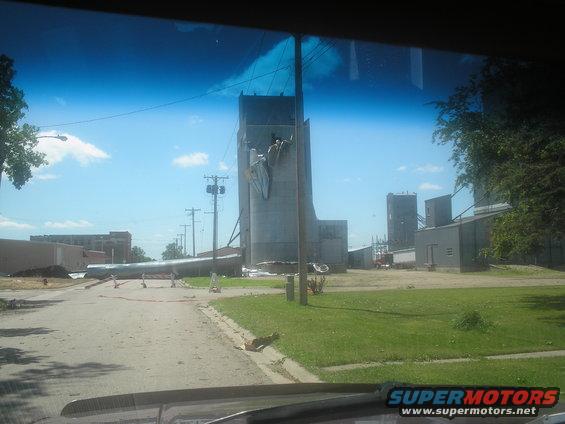 Damaged grain silo with debris scattered on a road under a blue sky