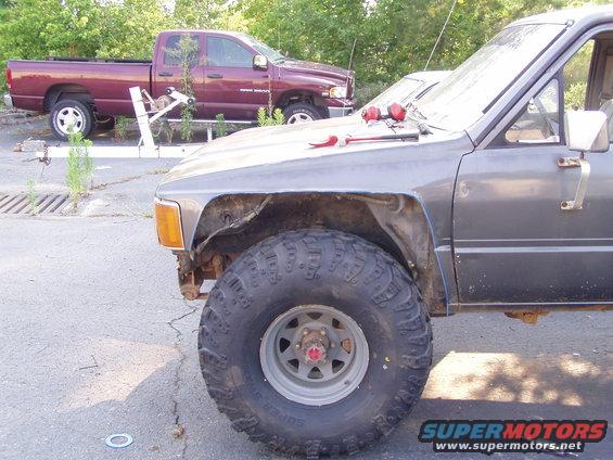 Gray truck front fender and large tire; maroon Dodge Ram pickup in background
