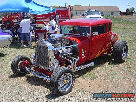 Red hot rod coupe with flames and a V8 engine, viewed from the front three-quarter angle