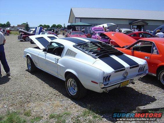 1967 Ford Mustang fastback with black stripes and louvers, parked at an outdoor car show