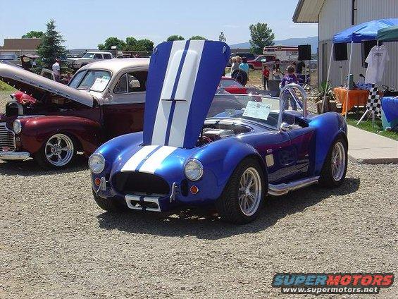 Blue AC Cobra replica with hood open, parked next to a maroon classic car