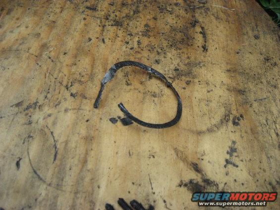 Curved, broken black rubber hose with white residue on a dirty wooden surface