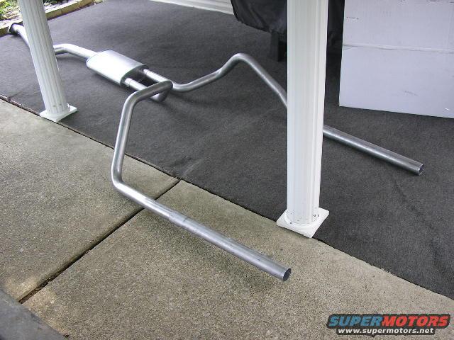 Exhaust system pipe and muffler assembly laid out on a dark mat between white posts