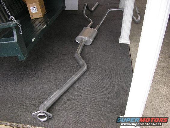 exhaust system laid out on a dark mat, with a box and part of a green bench in the background