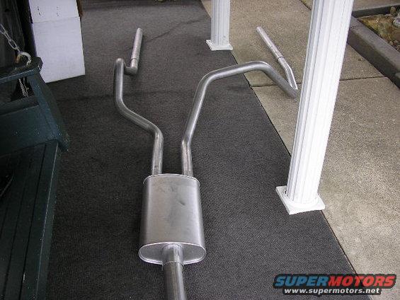 Dual exhaust system with oval muffler and bent pipes on dark carpet